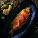 Delicately light steamed striped bass with ginger and scallion sitting atop a blue plate.