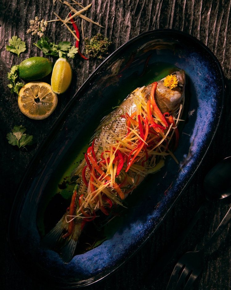 Delicately light steamed striped bass with ginger and scallion sitting atop a blue plate.