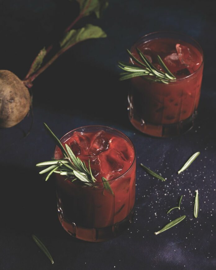 Beety Bloody Mary A beet-colored bloody mary on a black backgroound, garnished with a sprig of rosemary.
