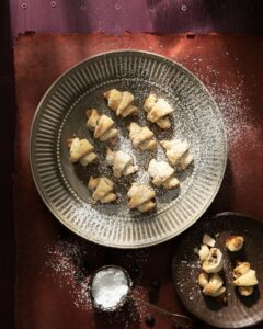 Chocolate Peanut Butter Rugelach lay on a plate covered in powered sugar.