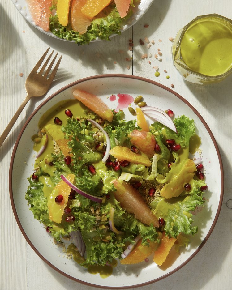 A white bowl contains a winter salad made with greens, pepitas, and plenty of sliced citrus fruit.