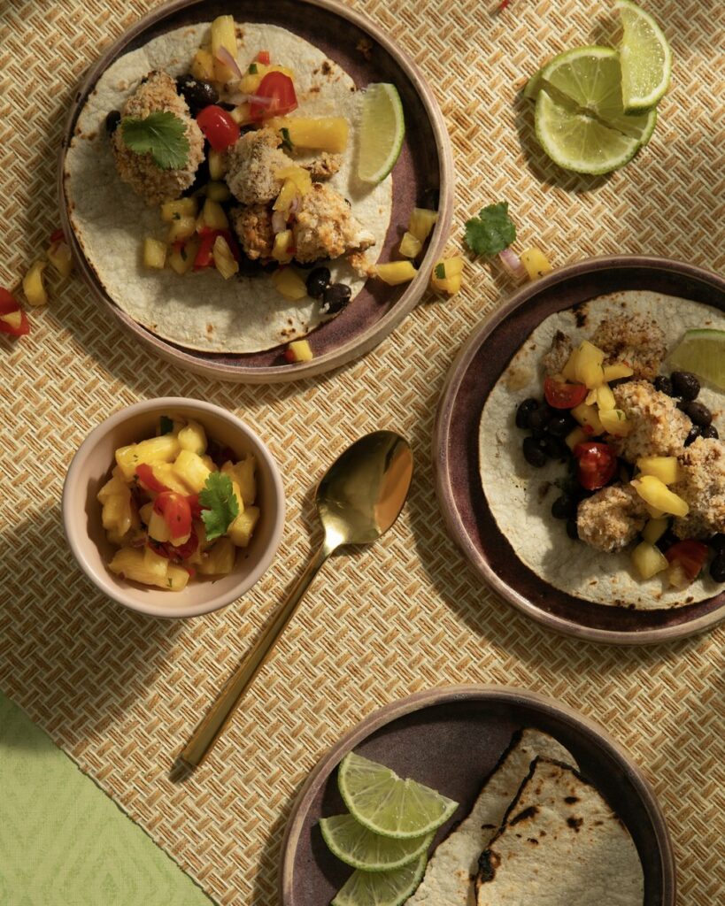 Meatless tacos Crispy Cauliflower Tacos. assembled on various plates with a small side of pineapple salsa on the table.