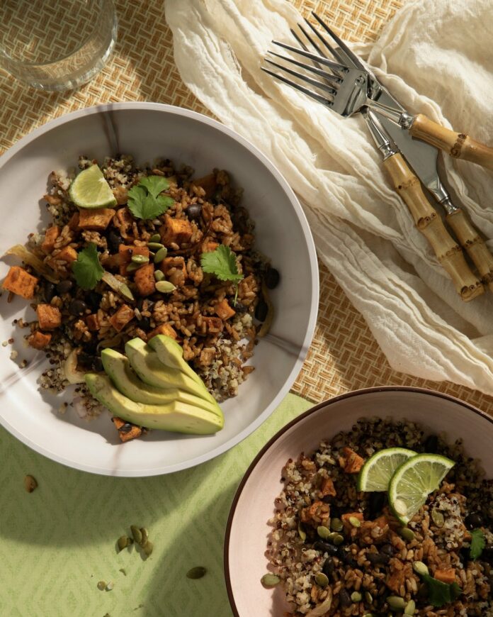 Two burrito bowls of sweet potatoes and grains sit in white bowls on a green background.