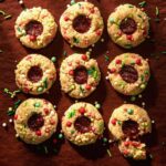 a variety of strawberry thumbprint cookies laid out on a red table and covered in Christmas sprinkles