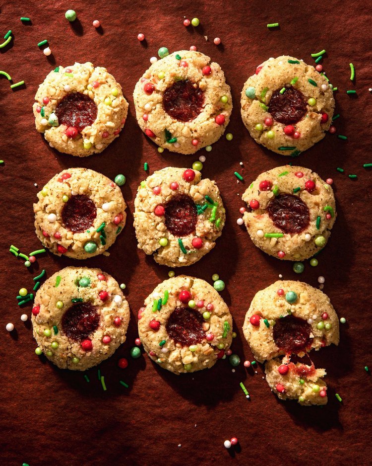 a variety of strawberry thumbprint cookies laid out on a red table and covered in Christmas sprinkles
