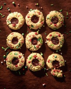 Strawberry rhubarb thumbprint cookies sit on a red background with sprinkles over top.