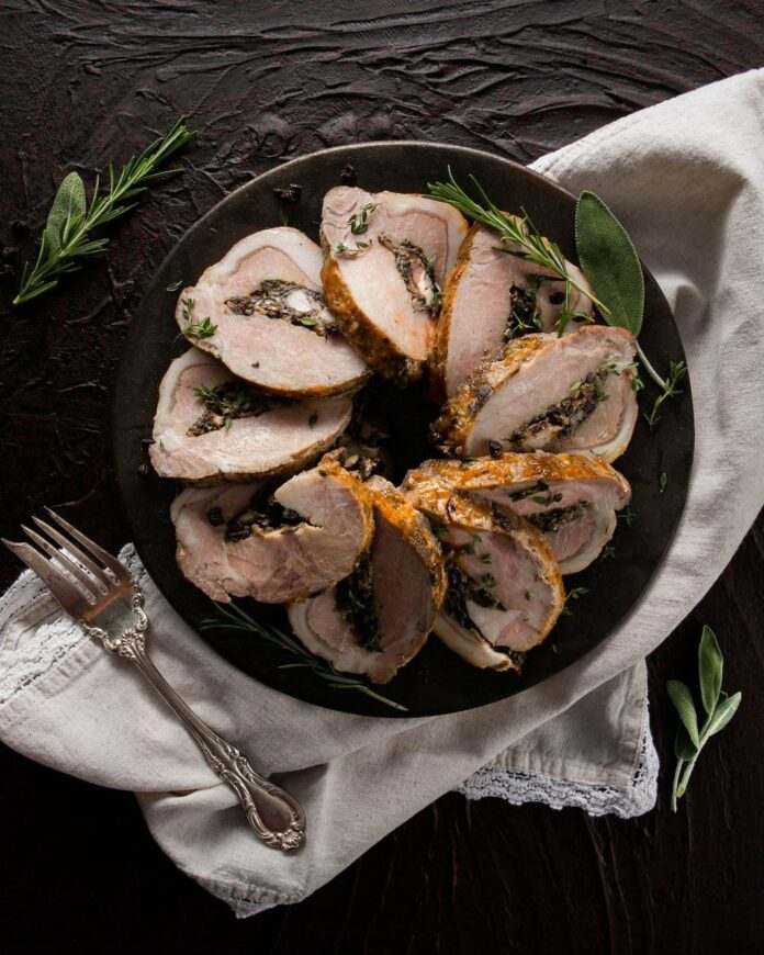 Sliced stuffed pork loin arranged in a circle on a black plate. pork loin recipe