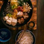 Sukiyaki with a side of white rice sits atop a wooden table with a woven mat.