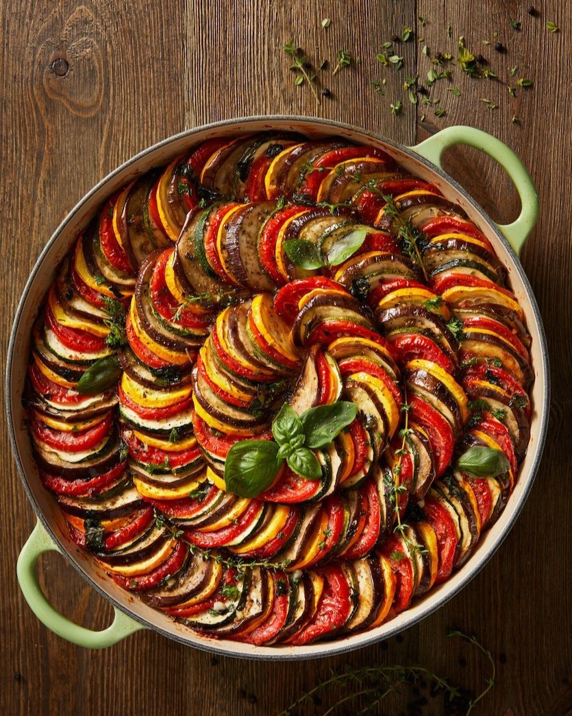 Spiral ratatouille with colorful layers of zucchini, eggplant, and tomatoes garnished with fresh basil, beautifully arranged in a green-handled dish.