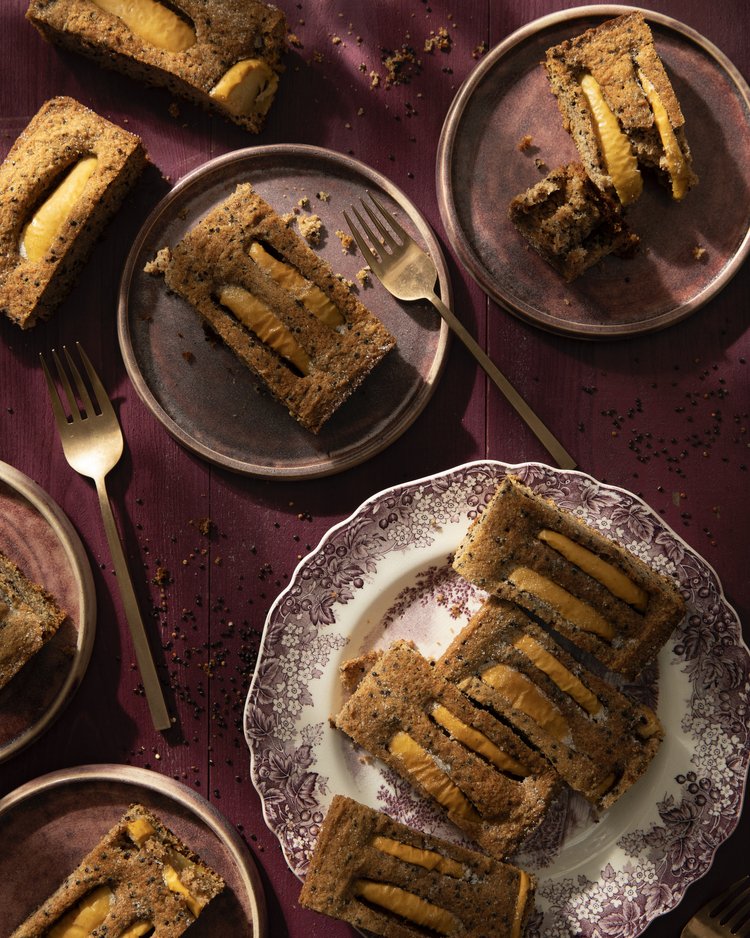 5 maroon plates sit on a deep purple table with slices of Apple Bourbon Quinoa Cake with forks beside each slice.