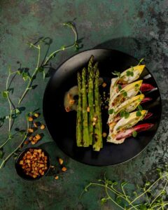 Grilled asparagus with green chile ricotta sits on a black plate.