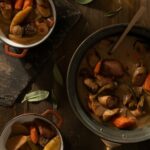 A large portion of beer brat stew sits next to smaller bowls of the hearty meal.
