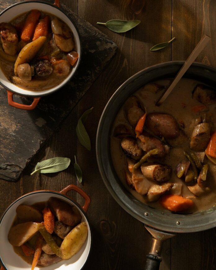 A large portion of beer brat stew sits next to smaller bowls of the hearty meal.