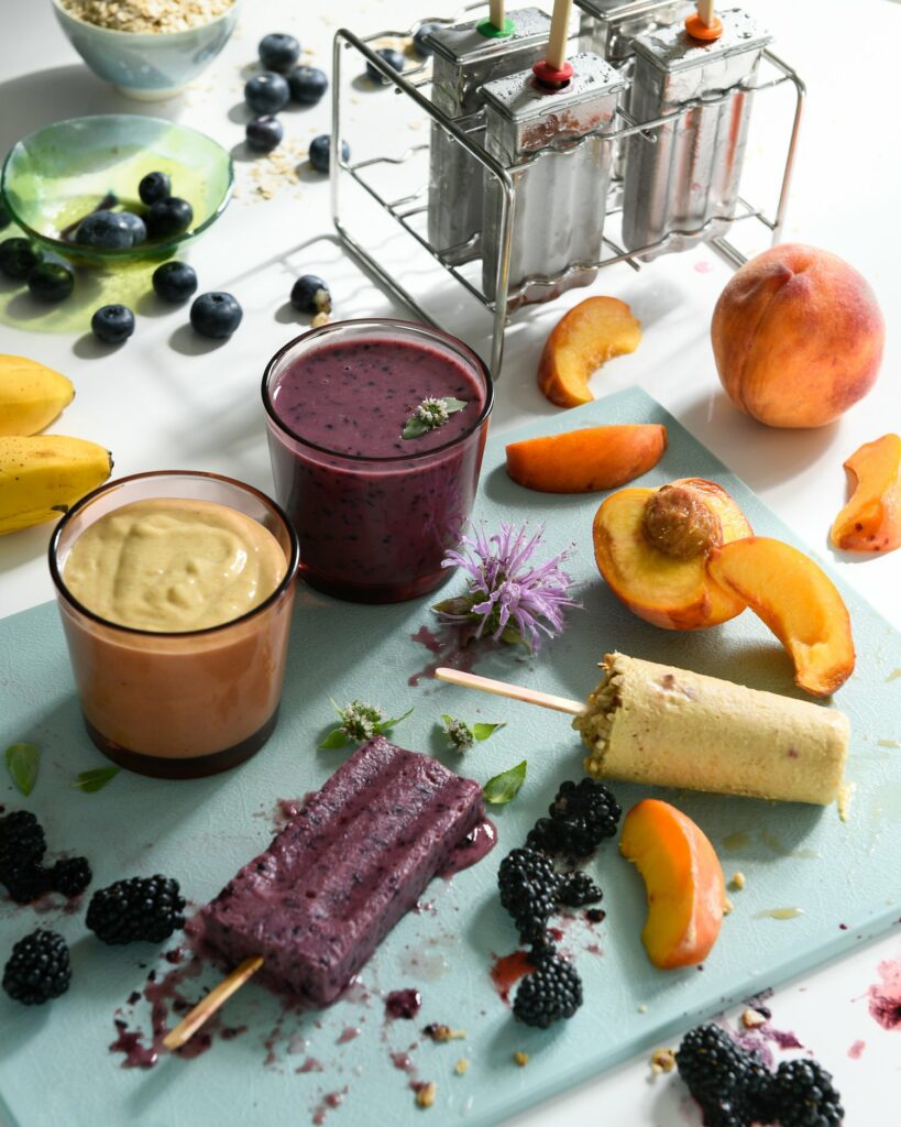 Two glasses of yellow and berry smoothies sit beside two smoothie popsicles in the same colors.
