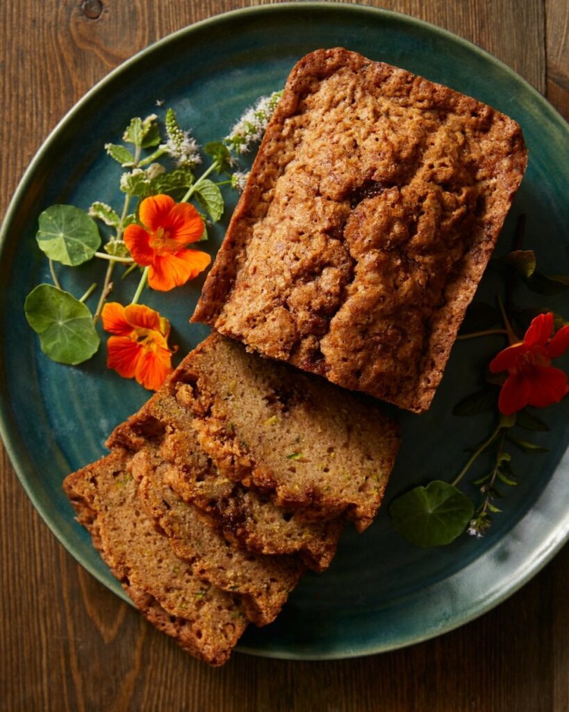 zucchini bread sits on a green plate, a few slices are cut from the front of the bread.