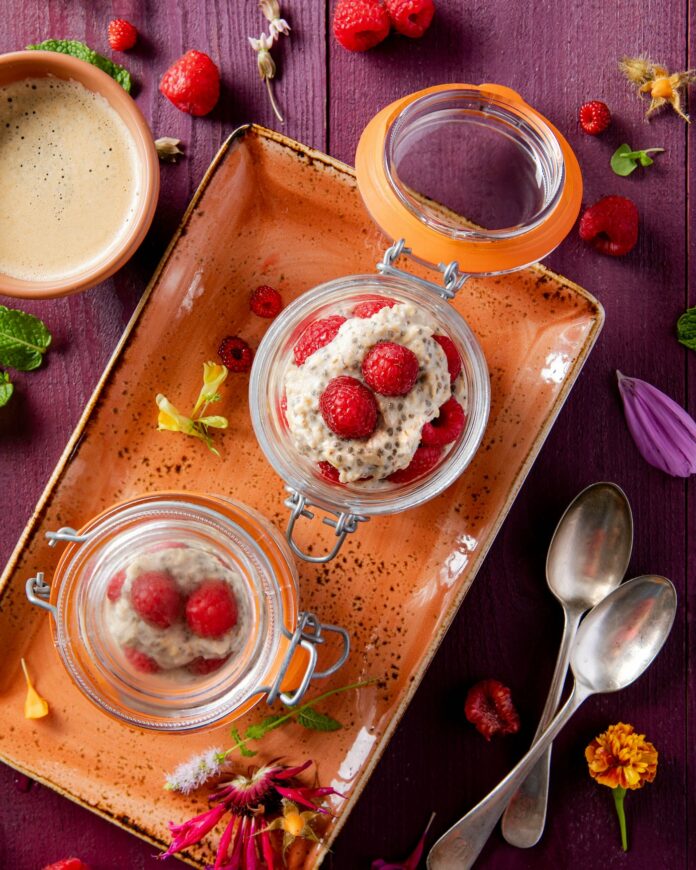 Chia Oat Parfait clear glass jars with overnight chia oats and raspberries set in an orange dish on a purple table