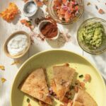 Chicken Quesadillas on a green plate accompanied by guacamole, sour cream, and pico.