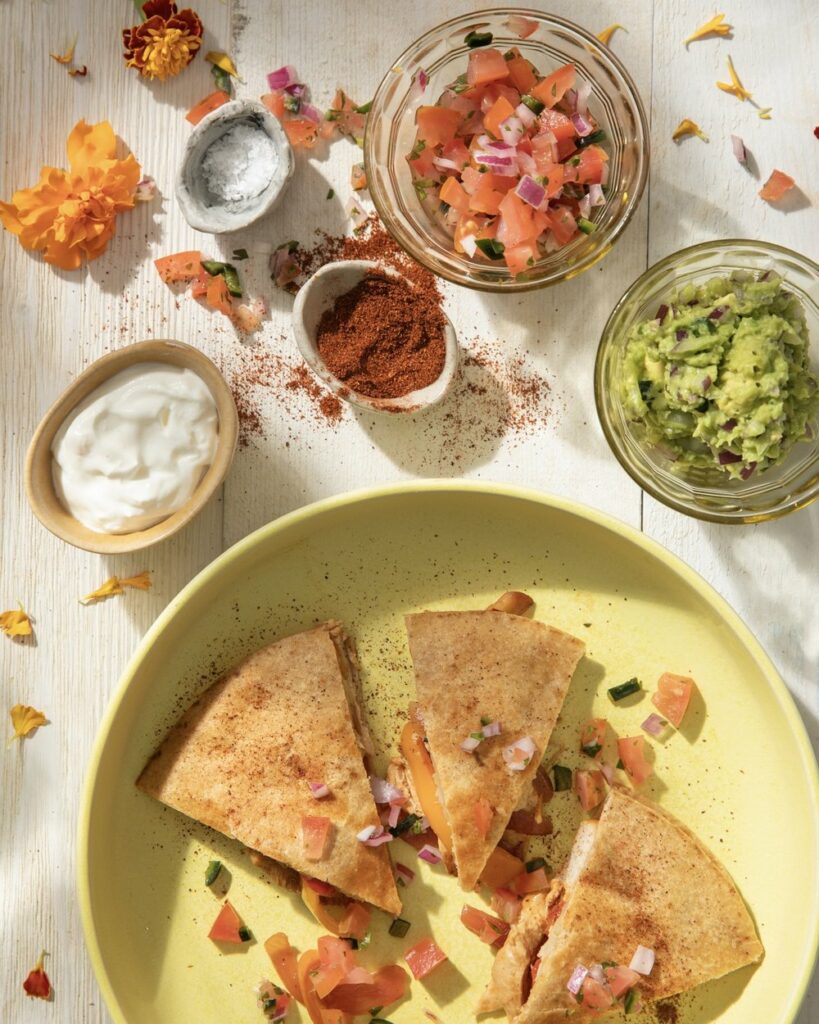 Chicken Quesadillas on a green plate accompanied by guacamole, sour cream, and pico.