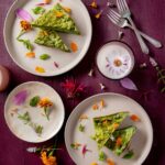 Green eggs adorned with flowers sit on three different plates.