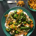 a plate of grilled zucchini in a yogurt sauce adn with a corn relish sits on a green plate witha. fork full above it.