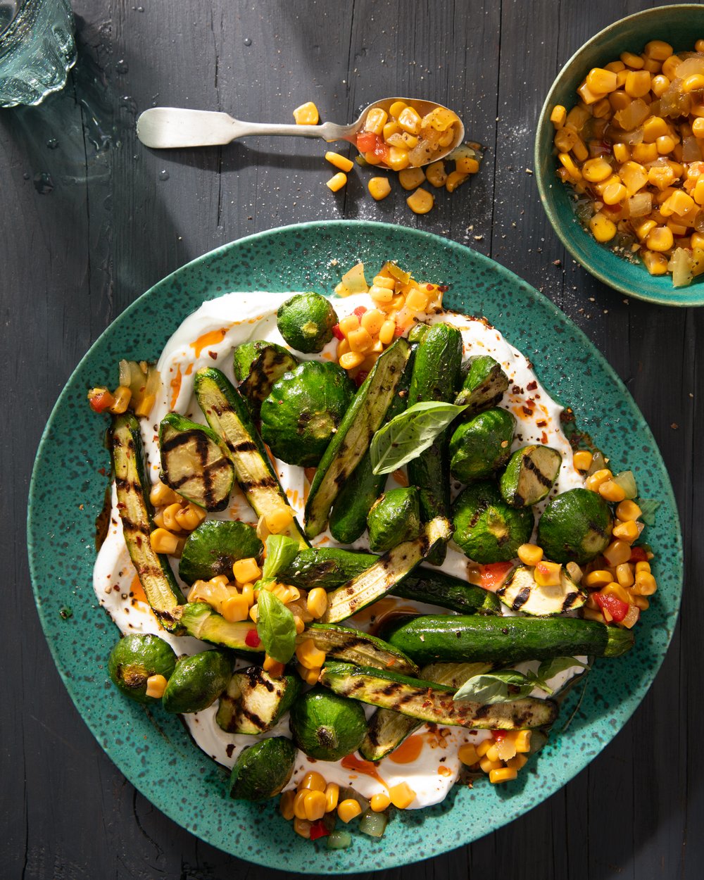 a plate of grilled zucchini in a yogurt sauce adn with a corn relish sits on a green plate witha. fork full above it. 