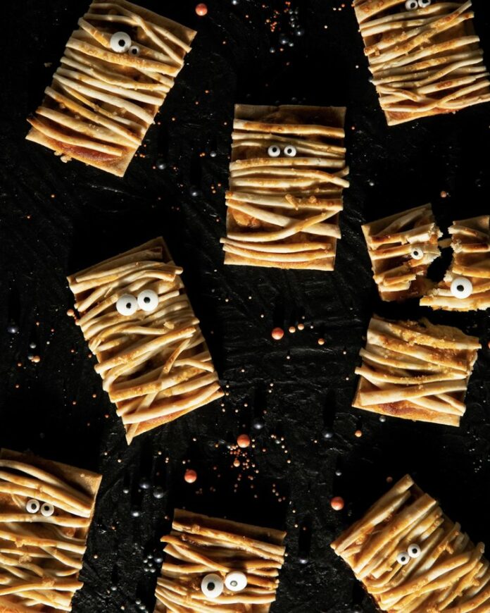 an aerial shot of eight Halloween Pumpkin Pastries laying on a black background with googly eyes attached