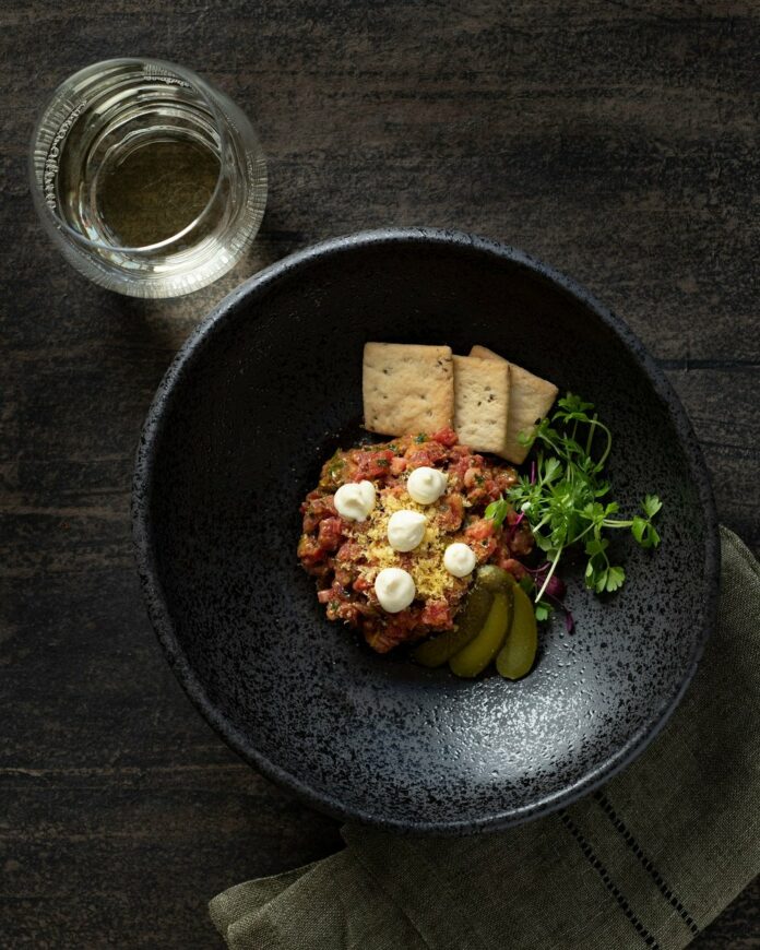 Aerial view of Prime Steak Tartare on a small, black, bowl looking plate.