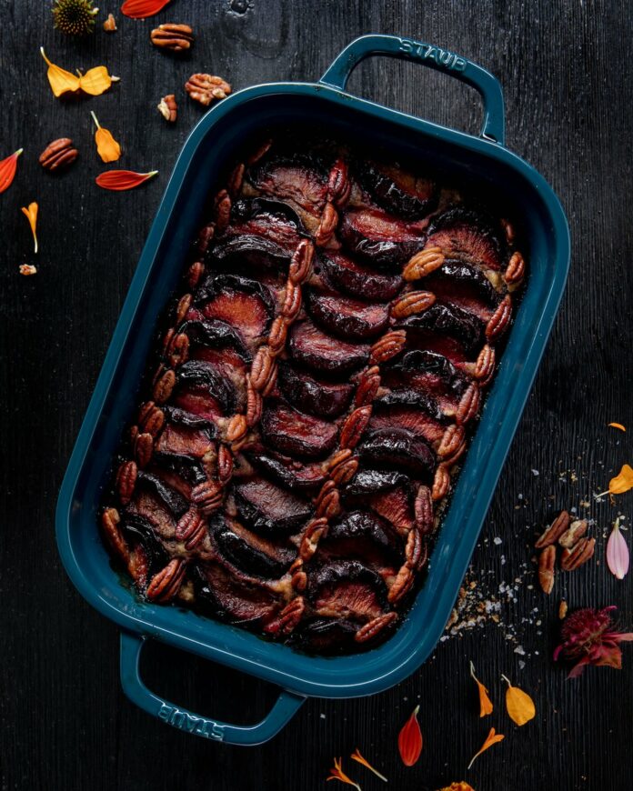 An aerial view of Orange Olive Oil Cake in a blue pan covered in plums and pecans.