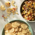 A bowl of peach and corn salsa sits to the top right of the frame, with a bigger bowl of tortilla chips in the bottom center.