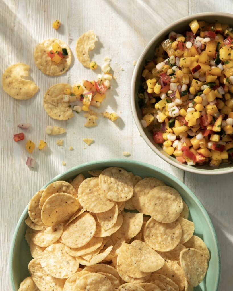 A bowl of peach and corn salsa sits to the top right of the frame, with a bigger bowl of tortilla chips in the bottom center.