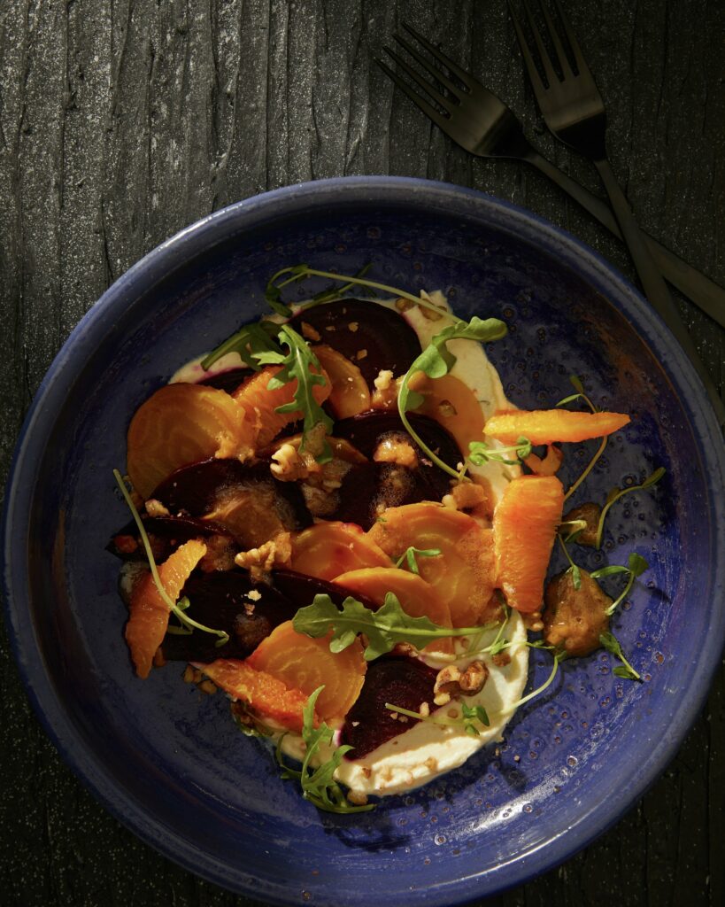 A blue plate on a wood table holds a winter salad made with roasted beets and other ingredients.