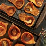 A variety of roasted squash on a baking sheet filled with orange slices and spices.