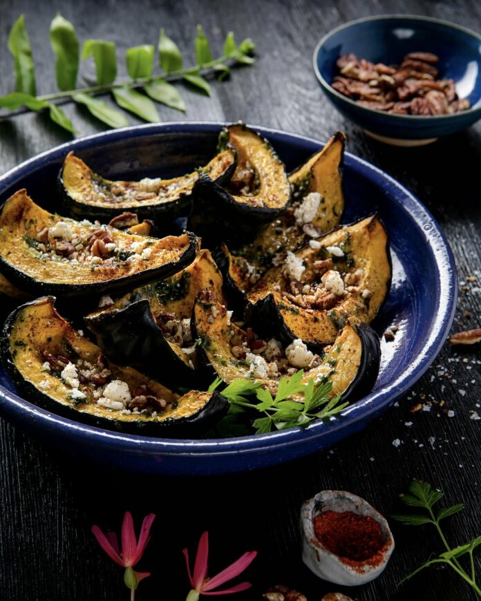 Roasted+Squash+with+Pesto+and+Crumbled+Goat+Cheese+TABLE+Magazine Wedges of acorn squash sit on a plate roasted with pesto and crumbled goat cheese on top.