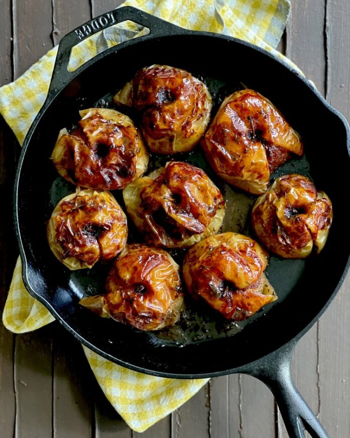 eight braised apples sit in a cast iron pan. braised apples recipe