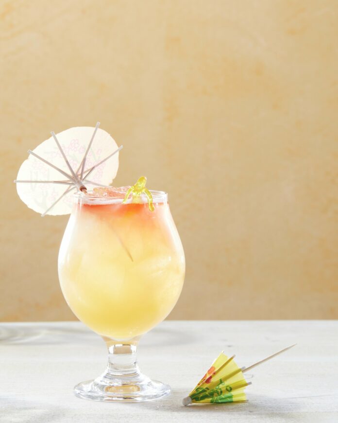 A yellow and orange rum cocktail garnished with a small paper umbrella.
