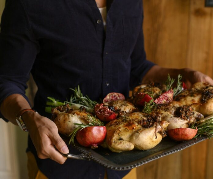 Herb-roasted Cornish hens stuffed with tart cherry, wild rice stuffing, and a pool of homemade gravy sit on a silver, rectangular serving tray.