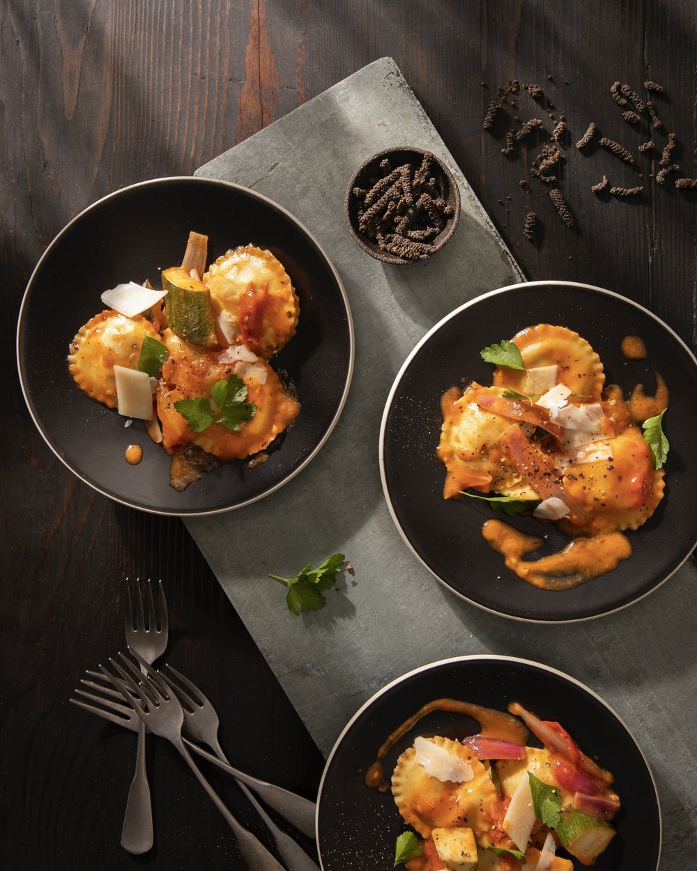 Summer veggie sauté with ravioli served on black plates, garnished with fresh herbs and shaved cheese.