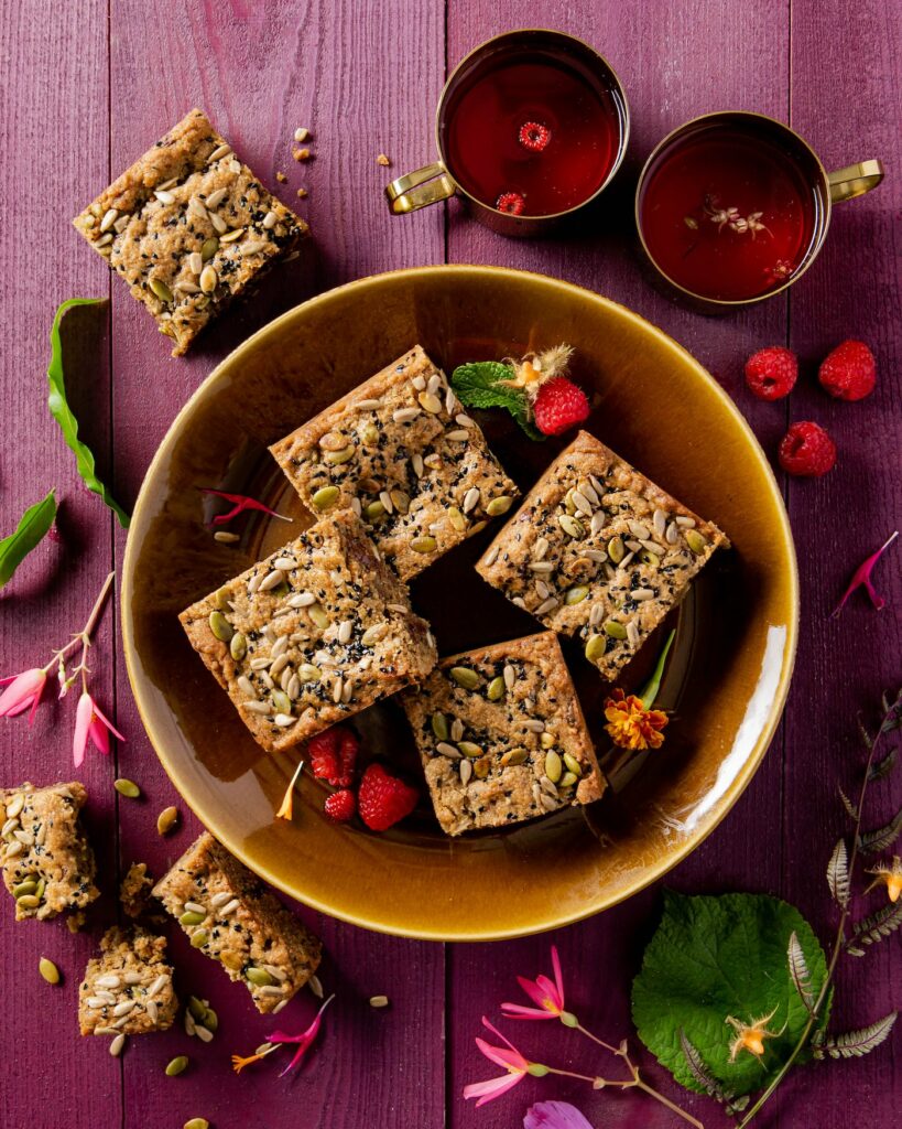 Four SunButter® Blondies sit in a brown bowl with raspberries sprinkled around the desserts.