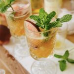 A white Nectarine Julep in a clear glass with mint garnish sits on a table.