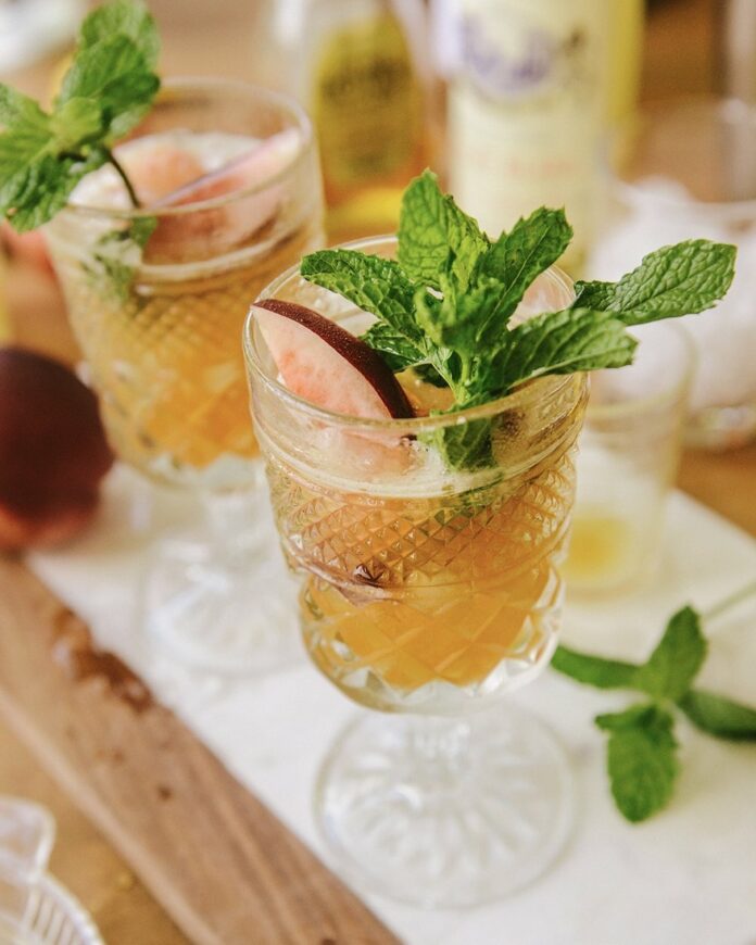 A white Nectarine Julep in a clear glass with mint garnish sits on a table.