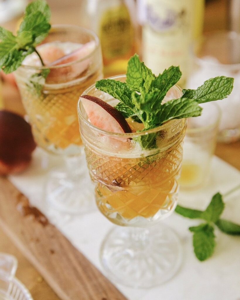 Two cocktail glasses with an orange liquid with a slice of fruit and fresh mint sticking out of the top.
