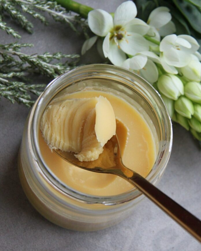 A spoon scoops a spoon-full of homemade butter out of a glass jar.