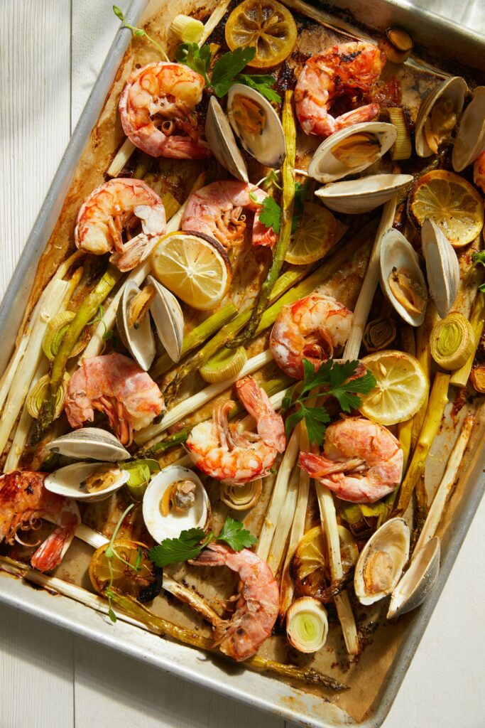Roasted Shrimp, Clams, Asparagus and Leeks on a sheet pan, garnished with lemon wedges. Sheet Pan Roasted Shrimp, Clams, Asparagus and Leeks Recipe