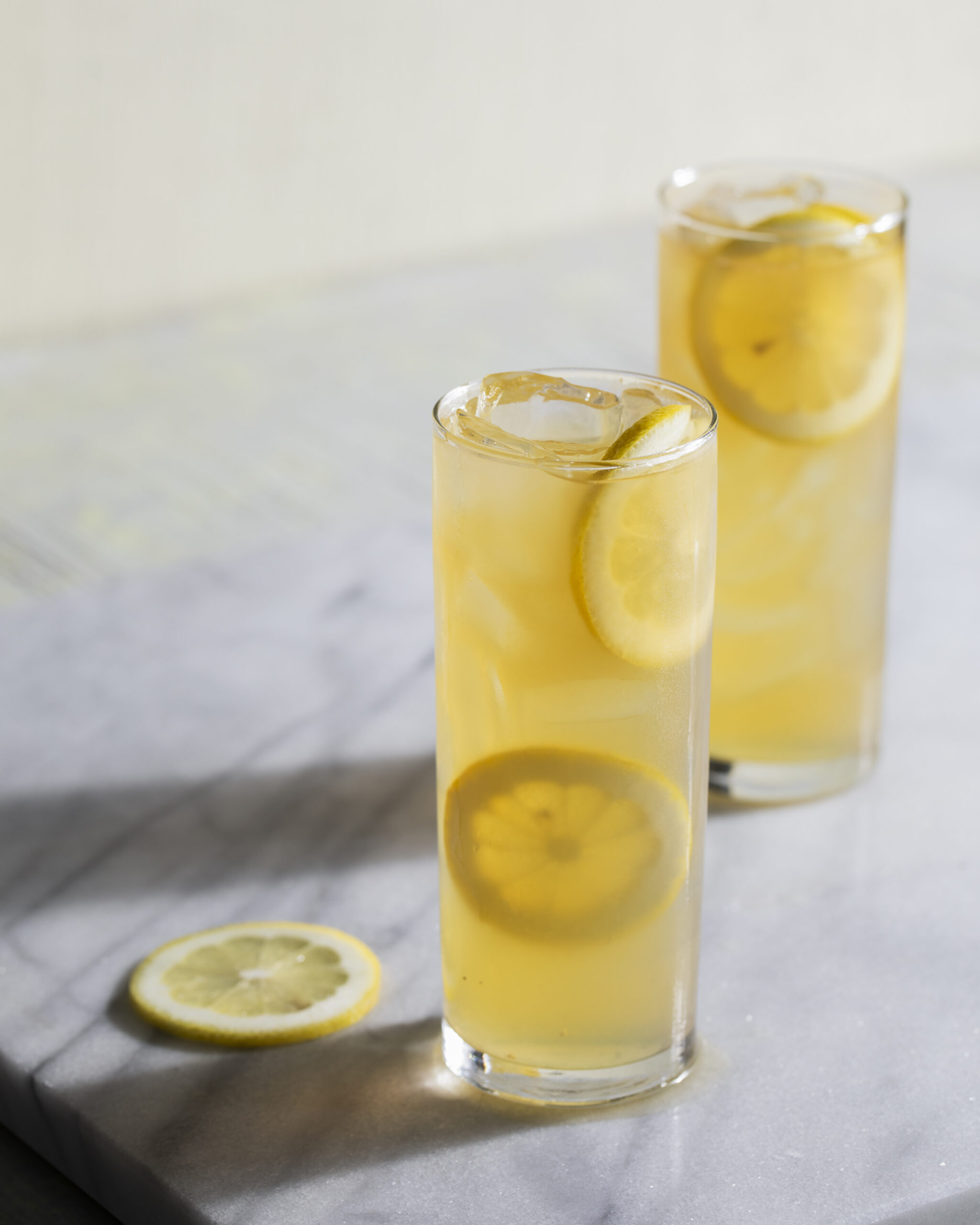 Two highball glasses, one slightly in front of the other, filled with a local riff on Lynchburg Lemonade. Bright yellow colors.