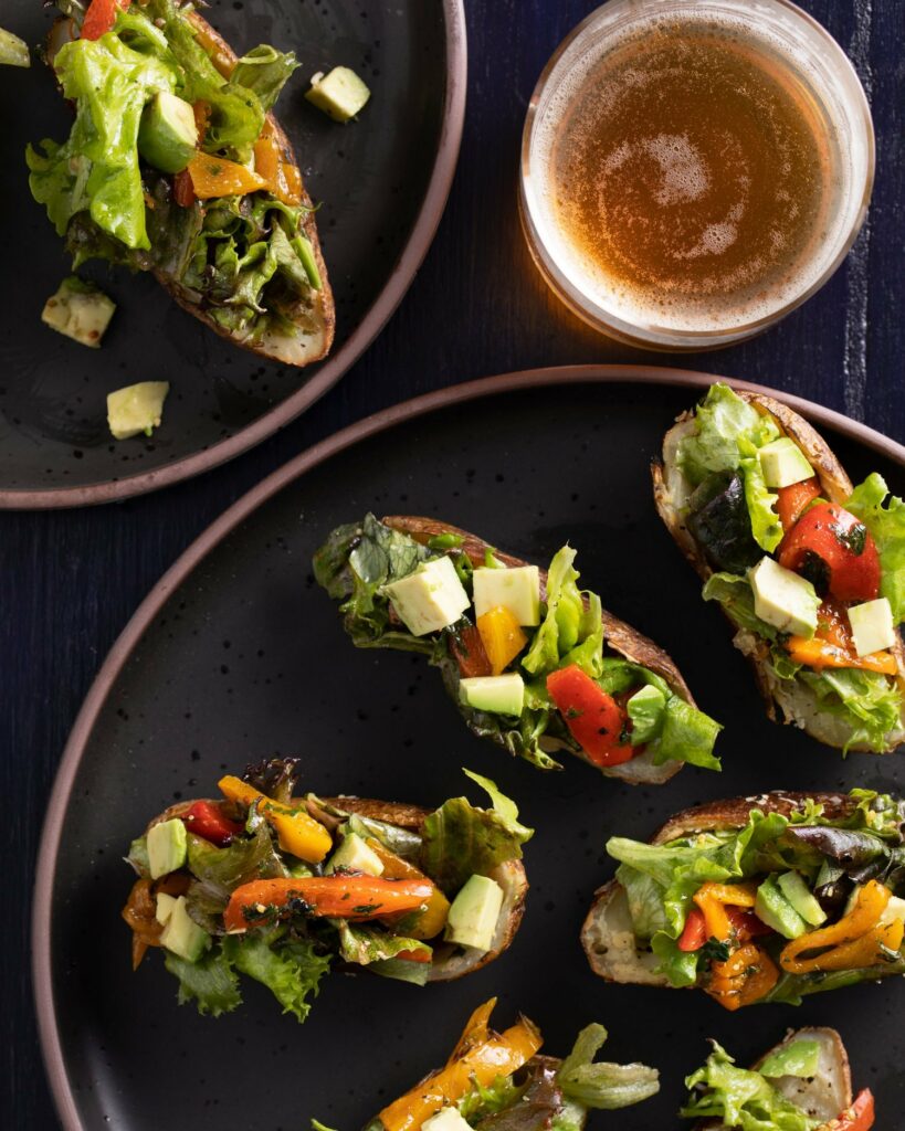 Small potato boats filled with salad on a black surface with a glass of beer on the side. 