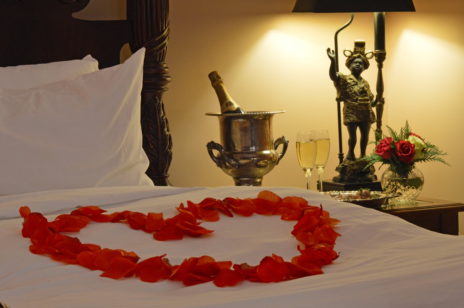 Rose Petals in the shape of a heart laid on a bed with white sheets.