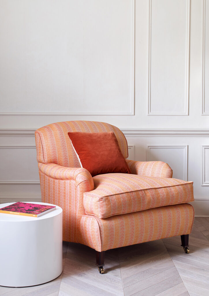 A photo of a peachy-pink chair with orange pillow by Cowtan & Tout illustrating a color design article. 