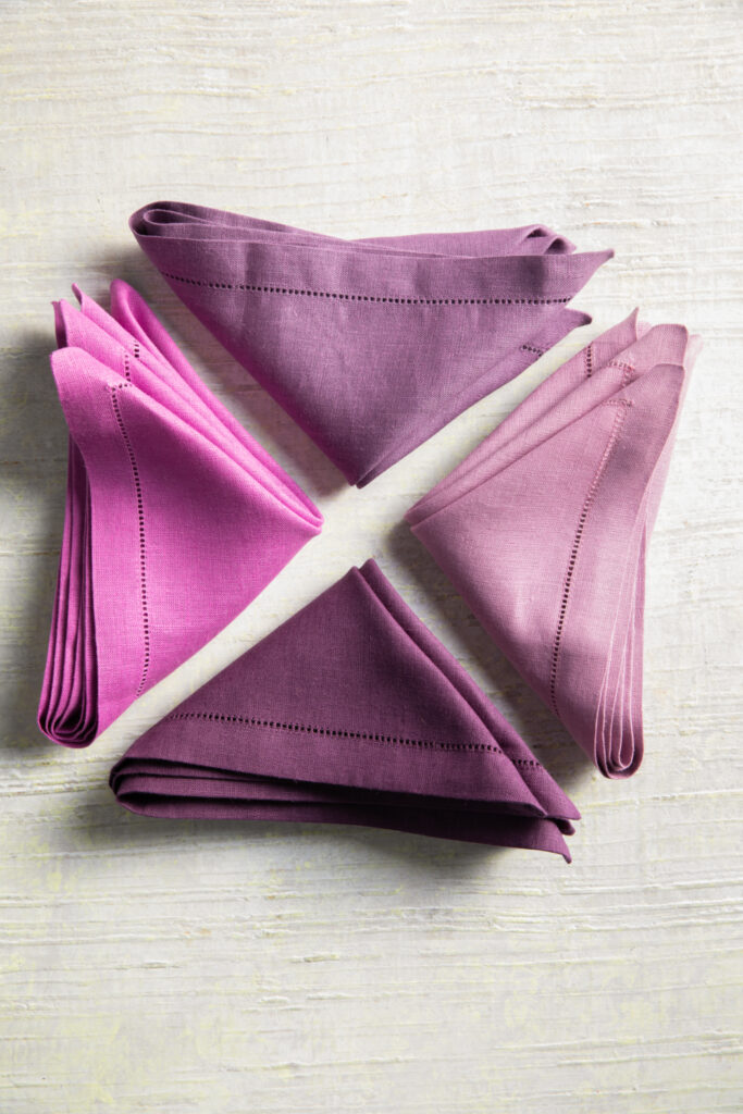 Purple linen Sferra napkins folded into triangles. 