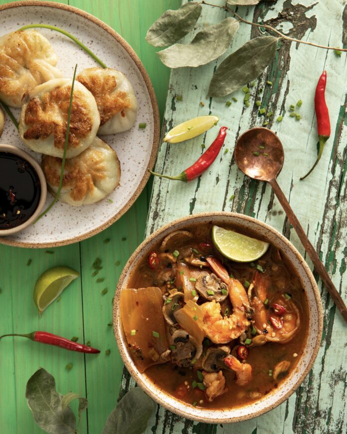 a tan plate with round dumplings and a bowl of red soup with shrimp on a green table