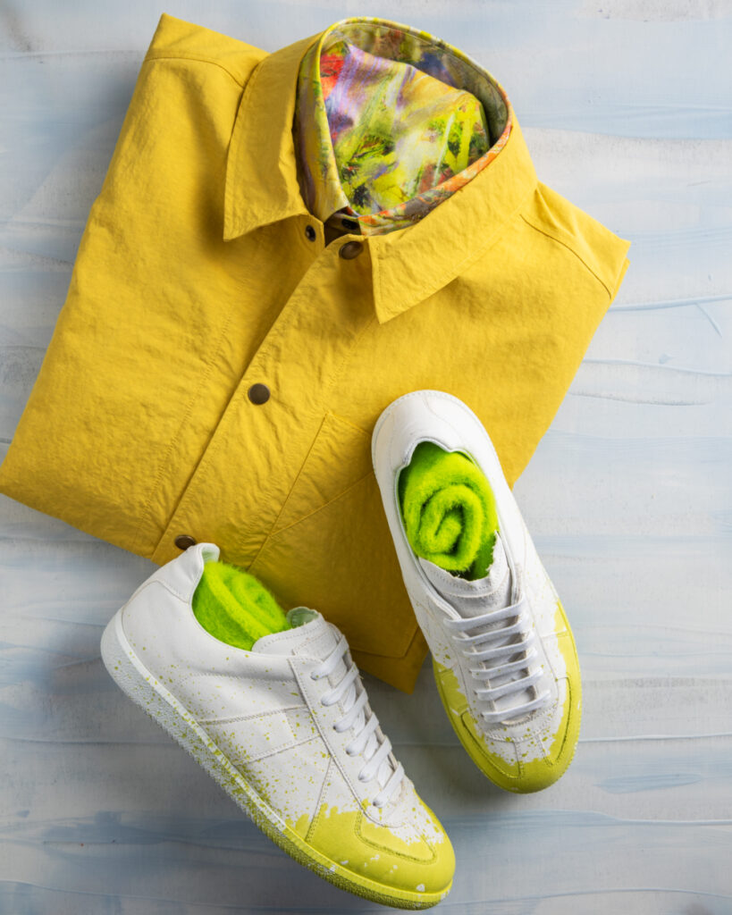 A photo of a folded yellow shirt and white sneakers with green socks tucked inside.